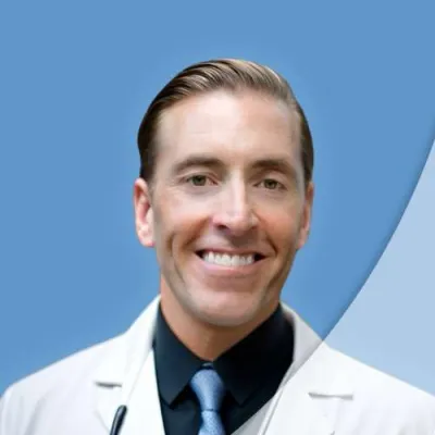 Smiling male doctor in white coat with stethoscope against a blue background.