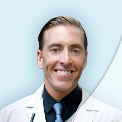 Smiling male doctor in white coat and tie with stethoscope on light blue background