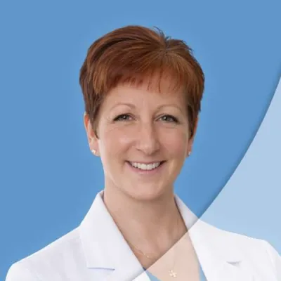 Smiling female medical professional with short red hair wearing a white coat against a blue background
