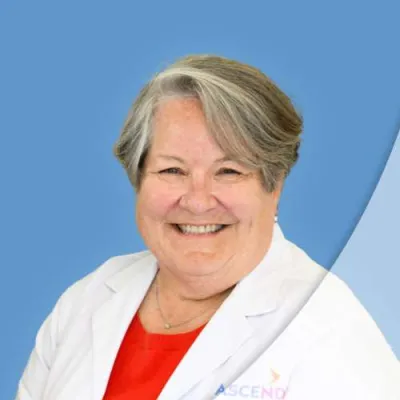 Smiling female doctor wearing white coat and red top with blue background in professional headshot.