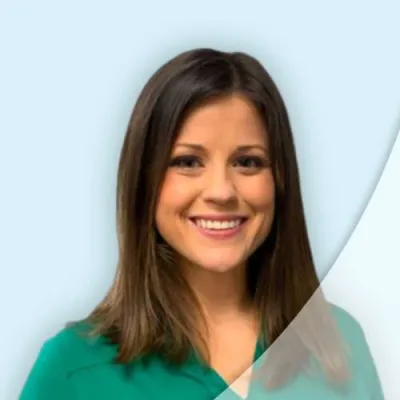 Smiling woman with straight brown hair wearing a green top against a light blue and white abstract background
