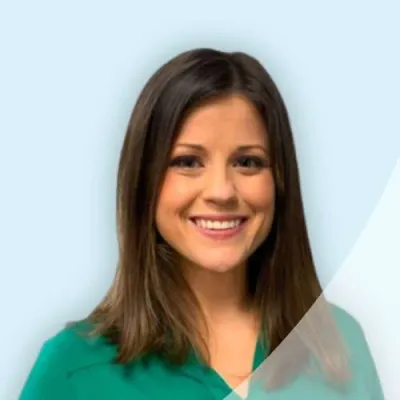 Smiling woman with brown hair wearing a green blouse against a light blue background