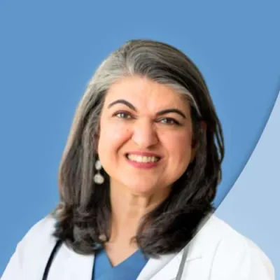 Smiling female doctor with salt-and-pepper hair wearing white coat and stethoscope on blue background