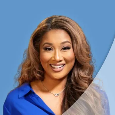 Smiling woman with long wavy hair in a blue shirt against a two-tone blue background.