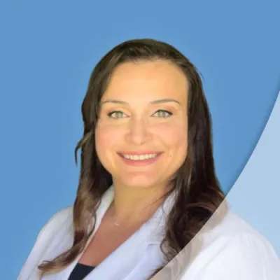 Smiling woman with long brown hair wearing a white lab coat against a blue background.