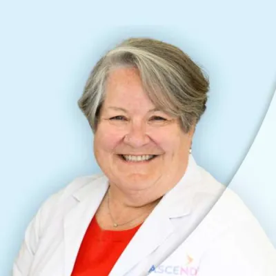 Smiling female doctor with gray hair in white coat and red top against light blue background.