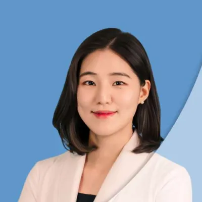 Professional woman in white medical coat against blue background, smiling confidently at the camera.