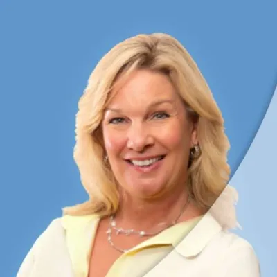 Smiling blonde woman wearing light yellow blouse and silver necklace against blue background