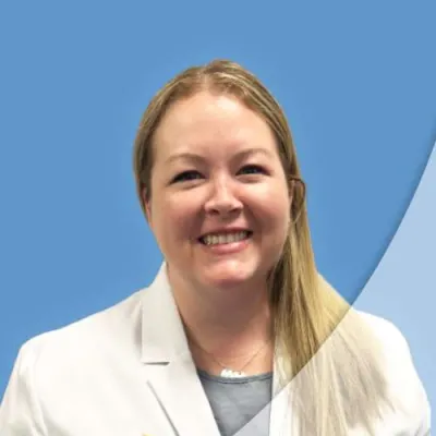 Smiling female medical professional wearing white Ascend Medical lab coat with blue background.