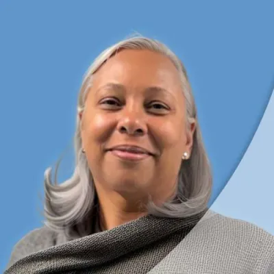 Smiling mature woman with gray hair wearing a textured gray shawl against a blue background.