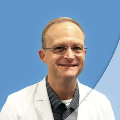 Smiling middle-aged man in glasses and white lab coat against a blue background