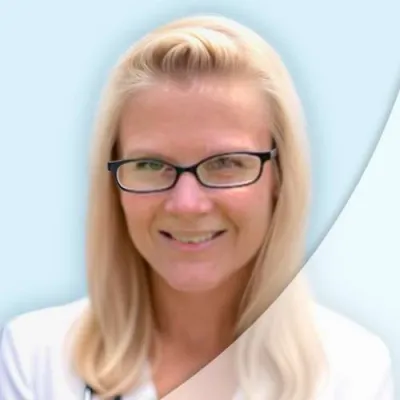 Blonde female doctor with glasses and stethoscope smiling against a light blue background.