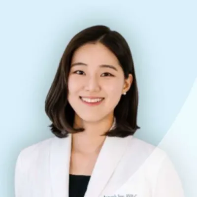 Smiling female healthcare professional wearing a white coat against a light blue background