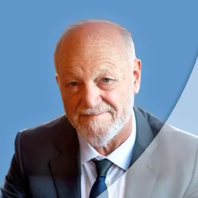 Portrait of an elderly man with a beard wearing a suit and tie against a blue background.