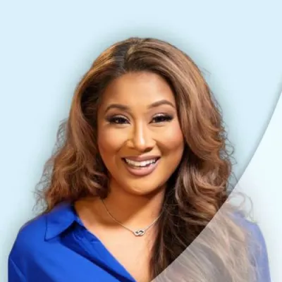 Smiling woman with long wavy hair wearing a blue blouse and silver necklace against a light background