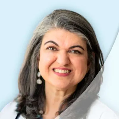 Smiling female doctor with gray hair, wearing a white coat and stethoscope on a light blue background