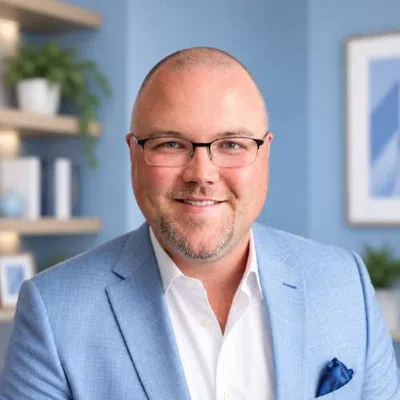 Smiling bald man wearing glasses and a light blue suit jacket with a white shirt in an office setting