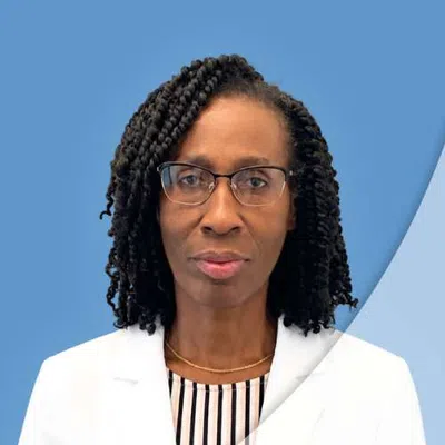 Professional woman with glasses and curly hair wearing a white blazer against a blue background.