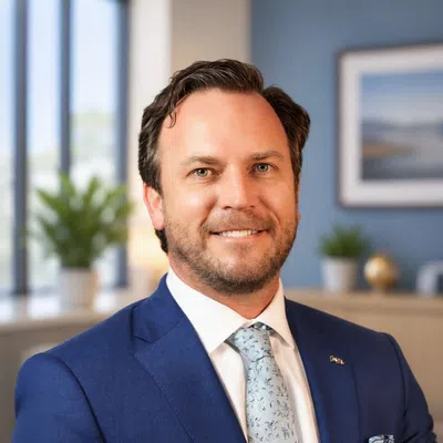 Smiling man in a blue suit with patterned tie and pocket square in a bright office setting.