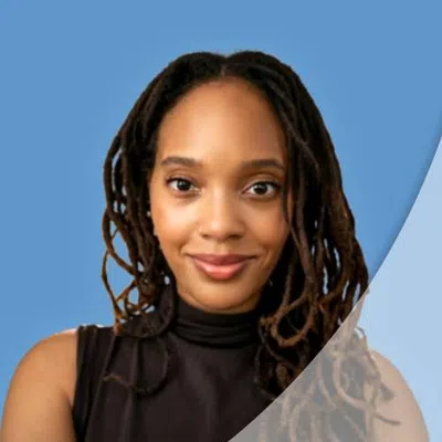 Smiling woman with long dark dreadlocks wearing a sleeveless black top against a blue background.