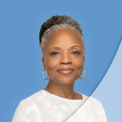 Confident older woman with gray braided hair wearing white blouse and hoop earrings on blue background