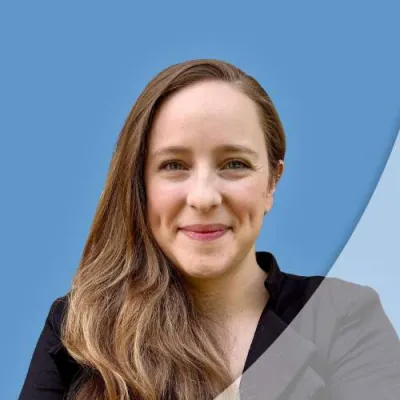 Smiling woman with long brown hair and dimples wearing a black top against blue and gray background.