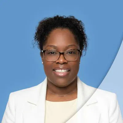 Professional woman wearing glasses and a white blazer smiling against a blue background.