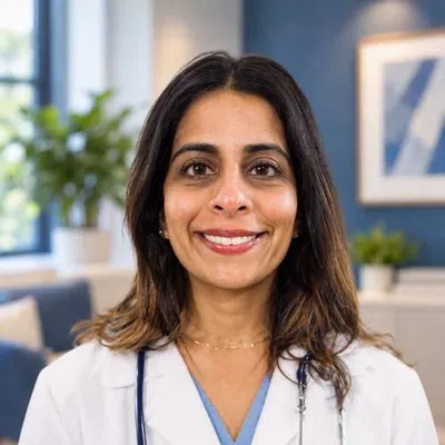 Smiling female doctor wearing a white coat and stethoscope in a bright, modern medical office setting.