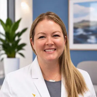 Smiling female medical professional in a white coat with Ascend Medical logo in a modern office setting.