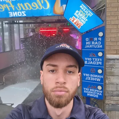 Man in Mr. Clean Car Wash uniform taking selfie inside a car wash with cleaning instructions visible.