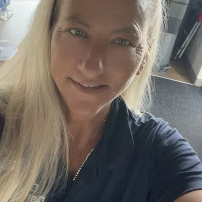 Smiling woman with blonde hair wearing a navy blue Clean Carwash uniform and name tag inside a car wash facility