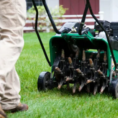 A person using a lawn aerator on a green grassy yard to promote healthy soil.