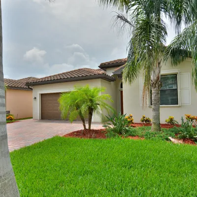 Modern single-story house with tiled roof, lush green lawn, palm trees, and a paved driveway