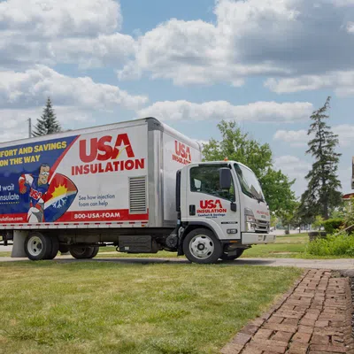 USA Insulation truck parked outside a suburban home, showcasing promotional wrap and a clear sky.