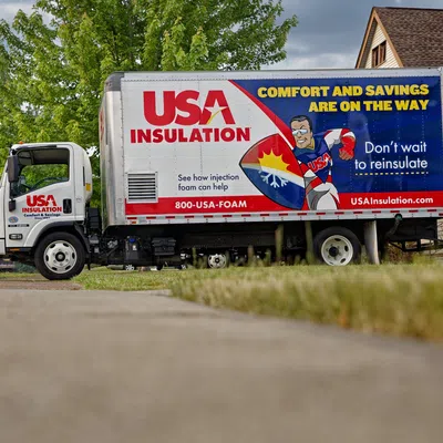 USA Insulation truck parked in residential driveway with company logo and slogan about reinulating homes.