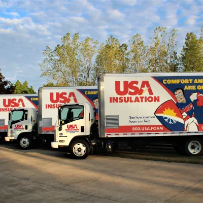 Three USA Insulation trucks parked under a blue sky, showcasing branding and contact information clearly.