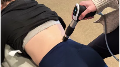 Therapist using a handheld device for pain relief treatment on a patient's lower back.