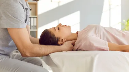 Therapist performing neck massage on a woman lying on a massage table in a bright room.