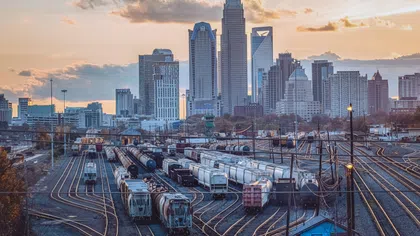 City skyline at sunset with multiple railroad tracks and parked freight trains in foreground.