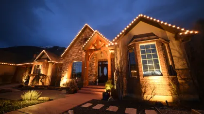 Beautiful warmly lit house with stone and wood accents during twilight and decorative roof lights.