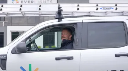 Man in white EverLights truck with ladder on roof parked outside building with EverLights sign.