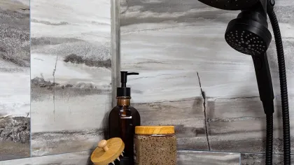 Black showerhead and toiletries on a gray marble corner shelf in a modern tiled bathroom