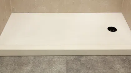 Modern shower base with beige tiled walls and gray floor, featuring a black circular drain on the right side.