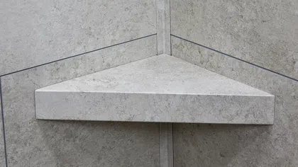 Triangular stone corner shelf mounted on a grey textured tiled wall in a bathroom or shower.