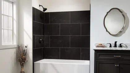 Modern bathroom with white bathtub, black tile shower wall, dark vanity, and decorative mirror with window light.