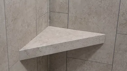 Triangular stone shower corner shelf mounted on beige tiled wall above white shower floor.