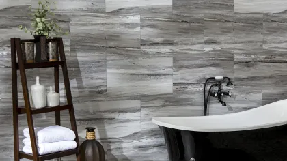 Modern bathroom with black clawfoot bathtub, gray stone tile wall, wooden shelf with towels and decorative vases