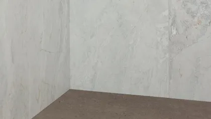 Corner of a shower with light gray marble walls and a textured dark gray shower floor with circular drain.