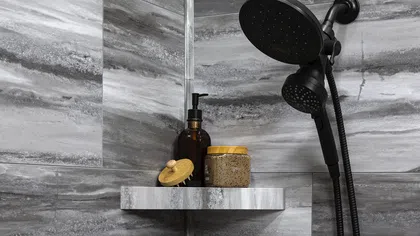 Corner shower shelves with gray marble tiles holding bath products and a black dual shower head.