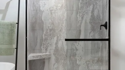 Modern bathroom shower with gray marble tiles, black metal frame, glass door, and green towel on black rack.